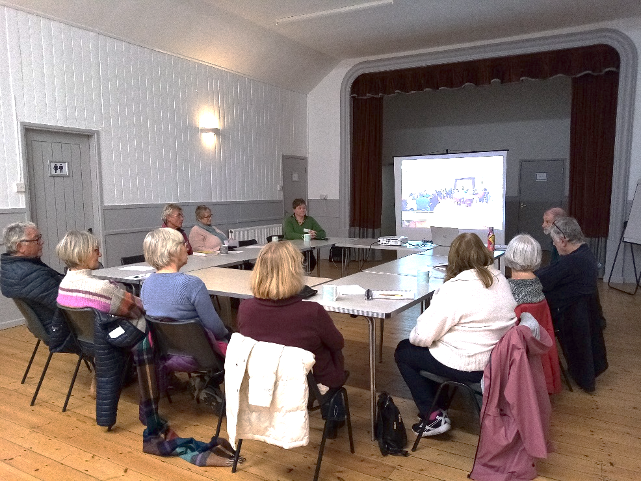 Village hall members sat round a table looking at a presentation on a screen