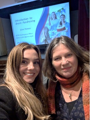 Tessa and Jamie smiling for a photo in front of a presentation screen