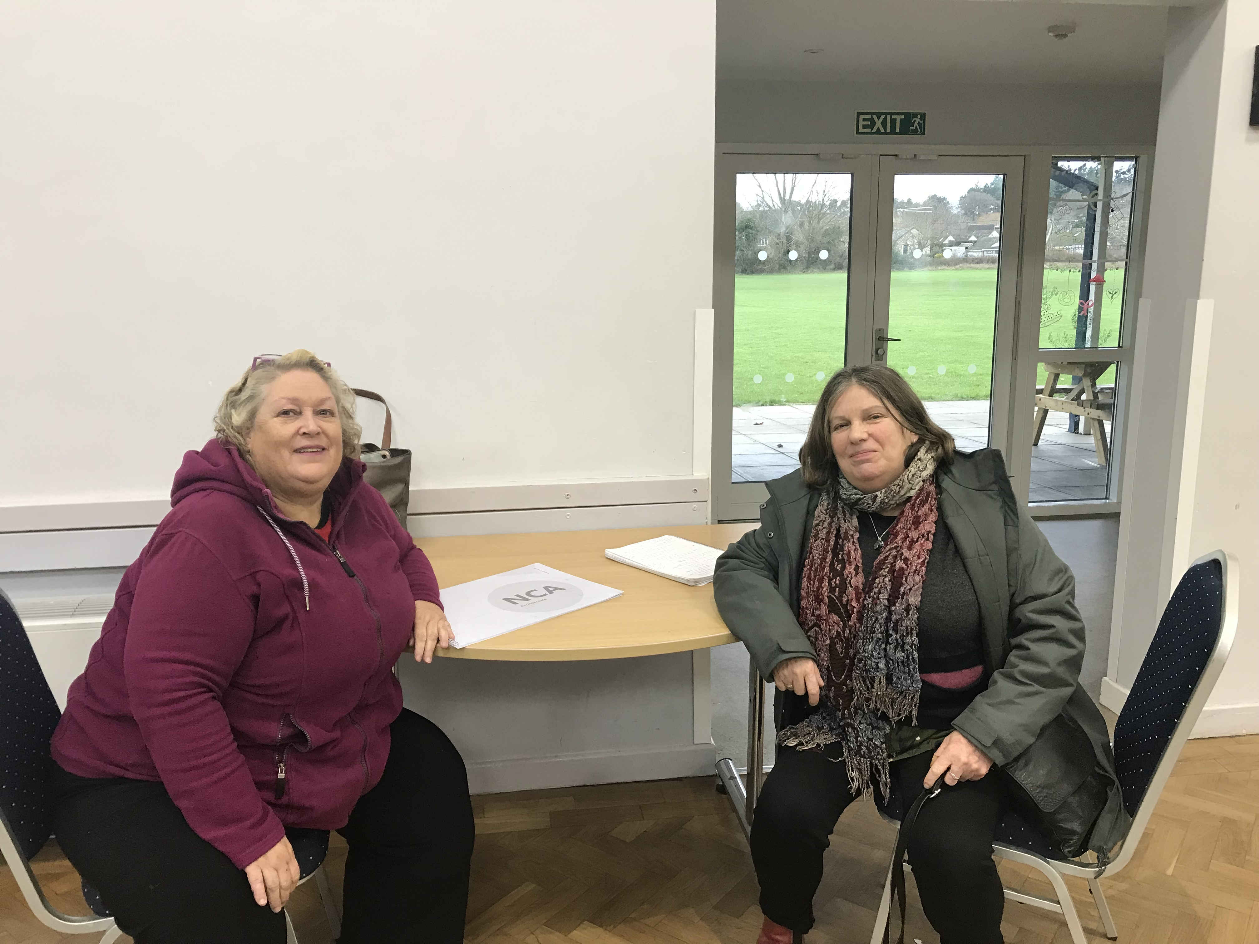 Tessa Hall from Community First Oxfordshire and the committee chair of Tackley Village Hall sit either side of a table smiling at the camera